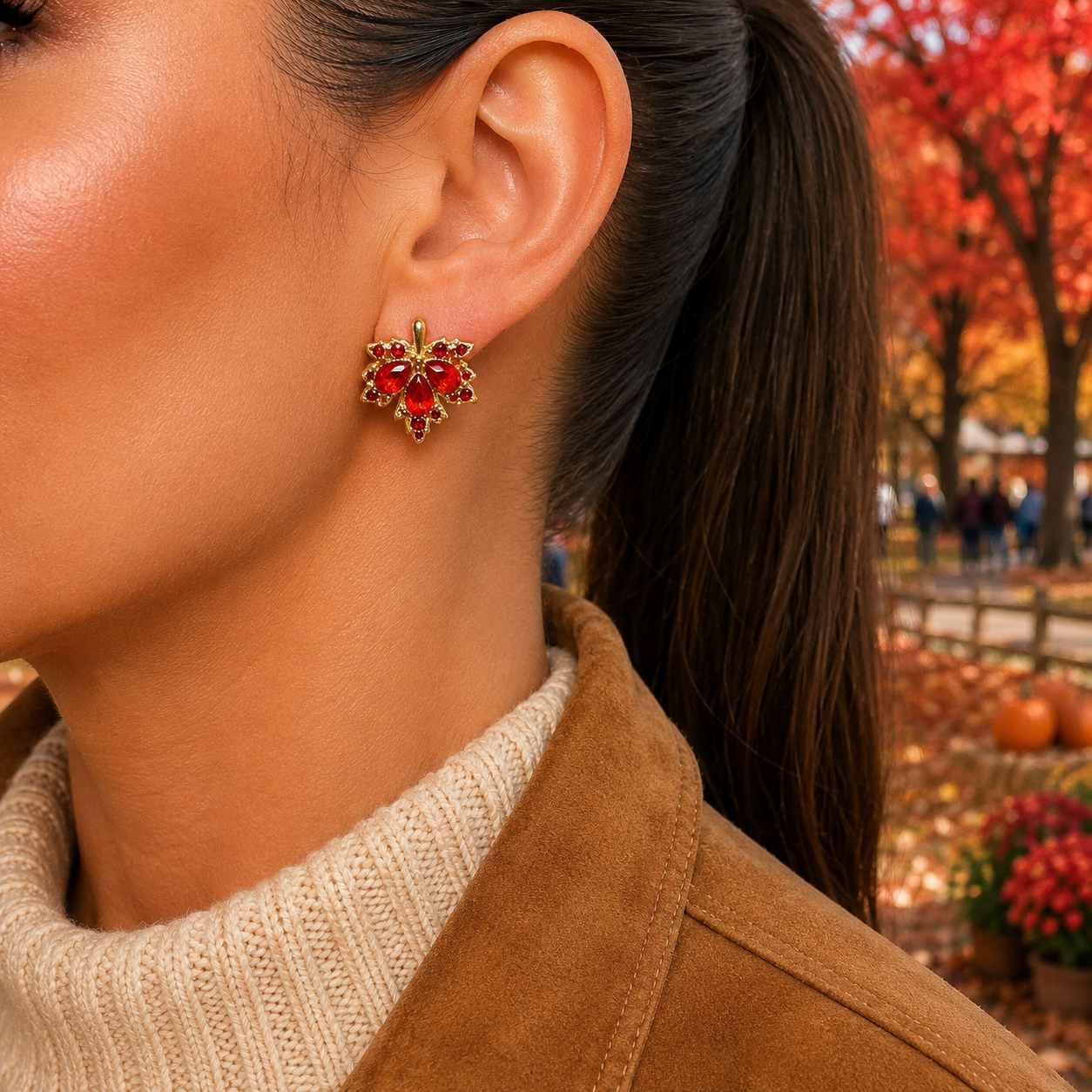 A close-up lifestyle shot of a woman wearing a Red Crystal Maple Leaf Earrings, set against an autumn park background with red trees and pumpkins.