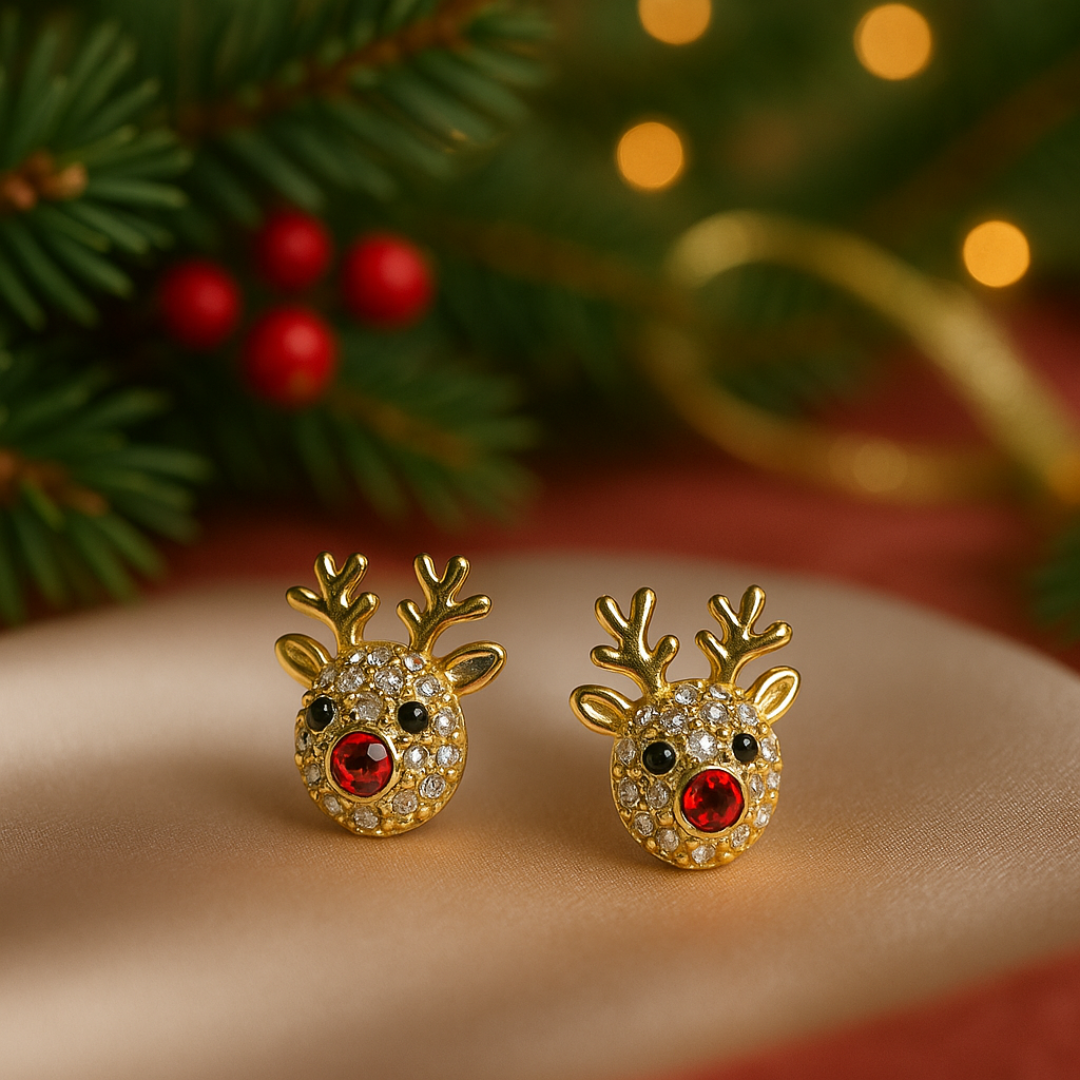 Gold reindeer-shaped earrings with red gemstones on a beige surface with Christmas decorations in the background.