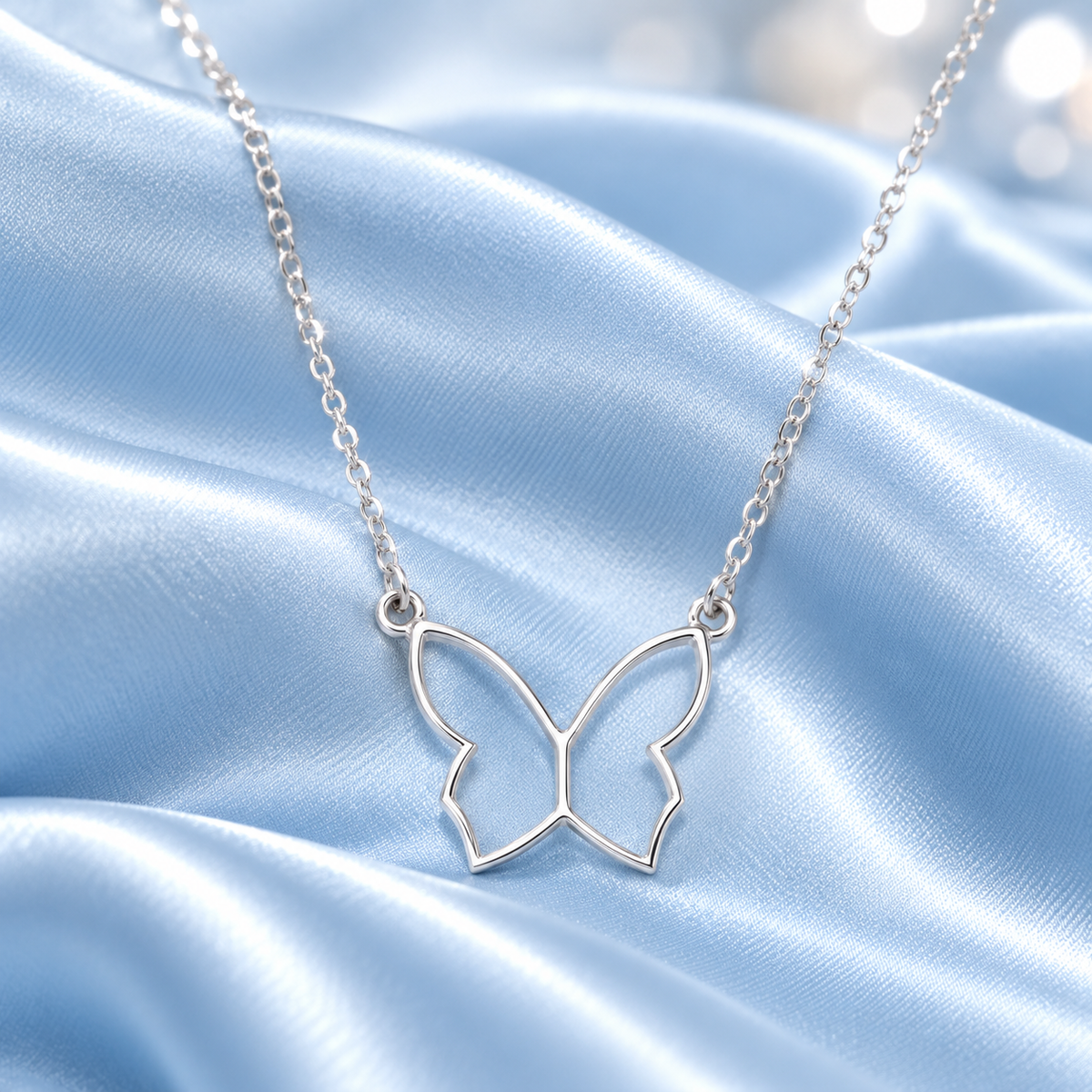 A silver butterfly-shaped pendant necklace on a delicate silver chain, displayed on a draped light blue satin fabric background.