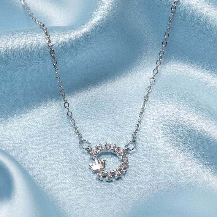 Silver Crowned Crystal Halo Necklace with a circular pendant featuring a crown on a light blue satin background