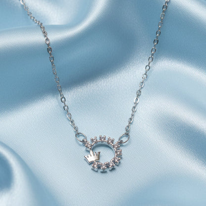 Silver Crowned Crystal Halo Necklace with a circular pendant featuring a crown on a light blue satin background
