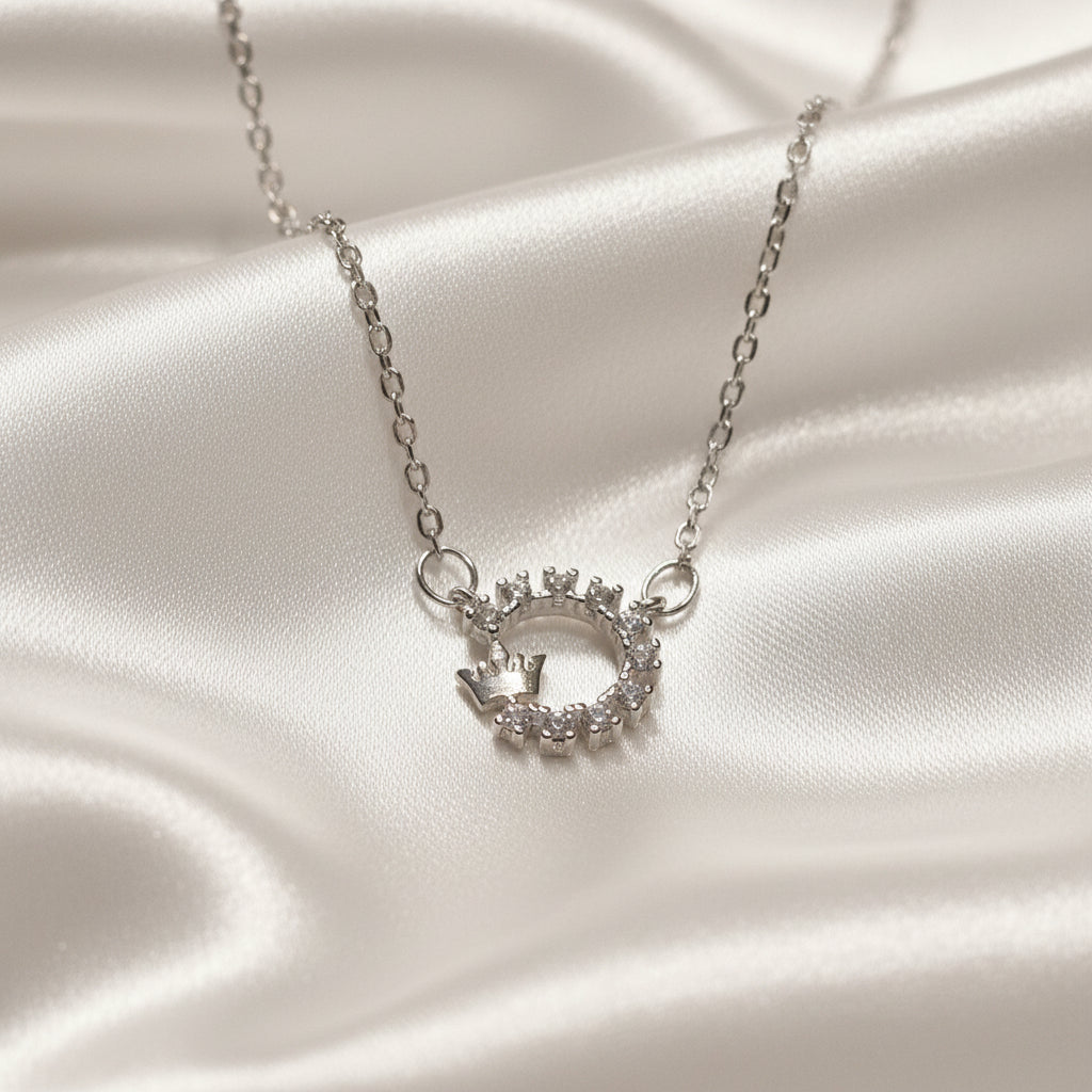 Silver Crowned Crystal Halo Necklace with a circular pendant on a satin surface