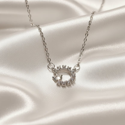 Silver Crowned Crystal Halo Necklace with a circular pendant on a satin surface