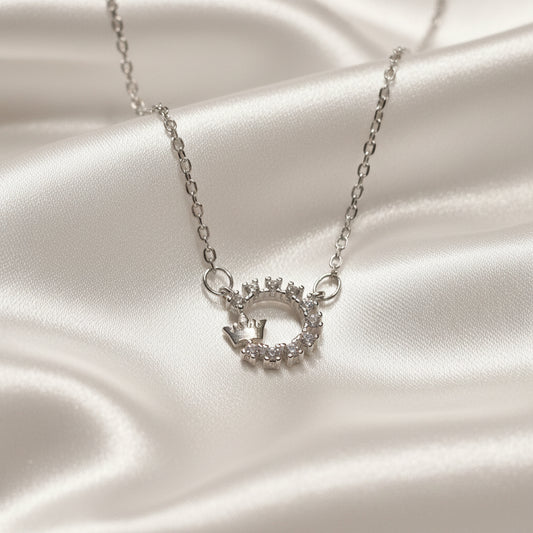Silver Crowned Crystal Halo Necklace with a circular pendant on a satin surface