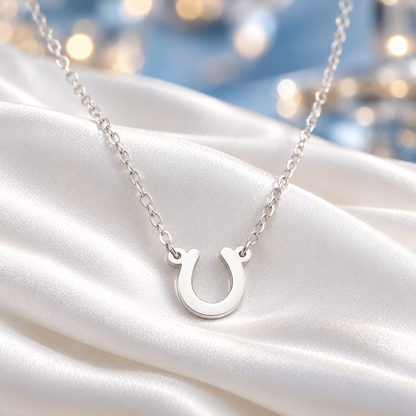 A silver Lucky Horseshoe Necklace on a delicate silver chain, draped elegantly over white satin fabric with a soft, blurred bokeh background.
