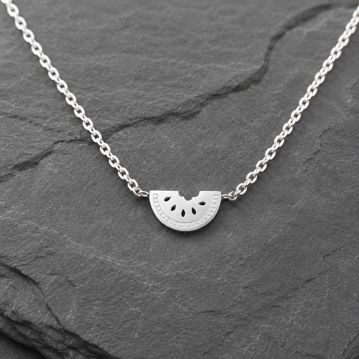 Silver Watermelon Slice Necklace on a dark stone surface