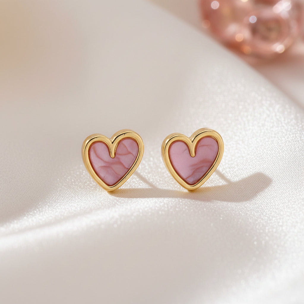 Soft Pink Pearlescent Heart Earrings on a textured beige surface.
