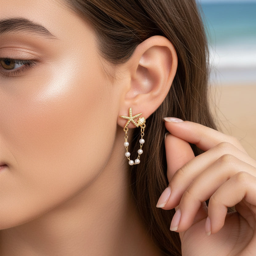Close-up of a woman wearing a Starfish Shell Pearl Earring, with a blurred beach background.