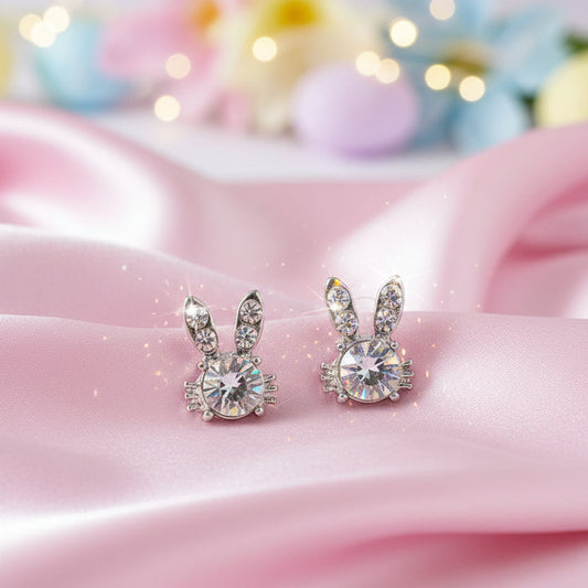 Sweet Bunny Sparkle Earrings with clear gemstones on a pink surface with blurred colorful background