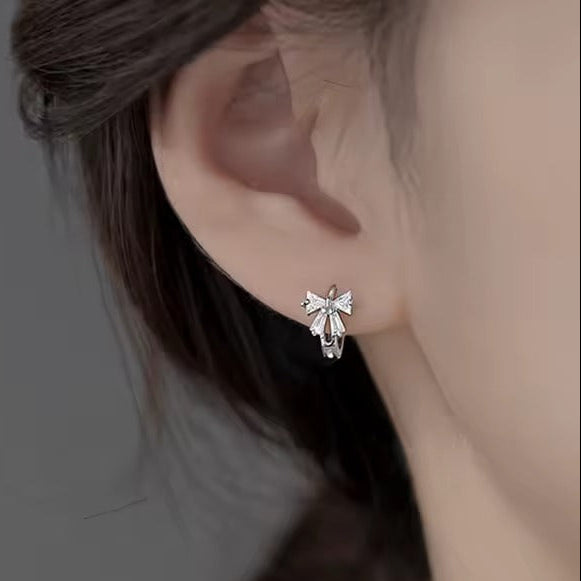Tiny Crystal Ribbon Earrings worn by a person with a blurred background
