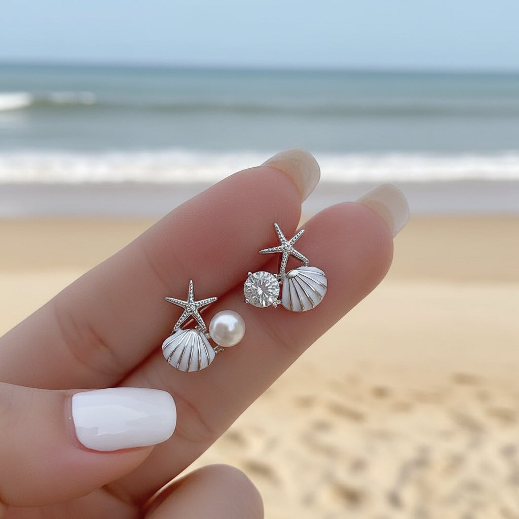 White Shell Pearl & Crystal Starfish Earrings on a hand against a light background.