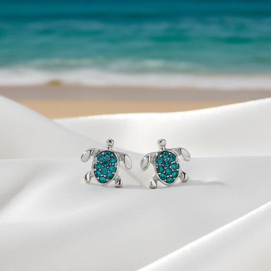 Aqua Pavé Sea Turtle Earrings with beach background