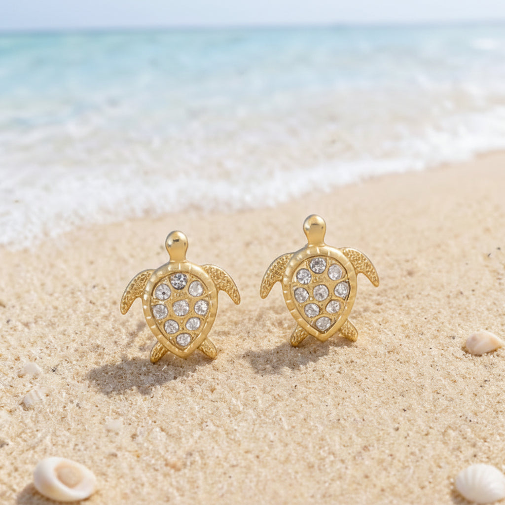 Gold Pavé Sea Turtle Earrings on a sandy beach.