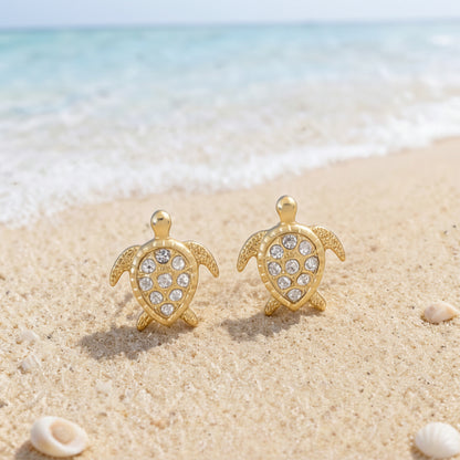 Gold Pavé Sea Turtle Earrings on a sandy beach.