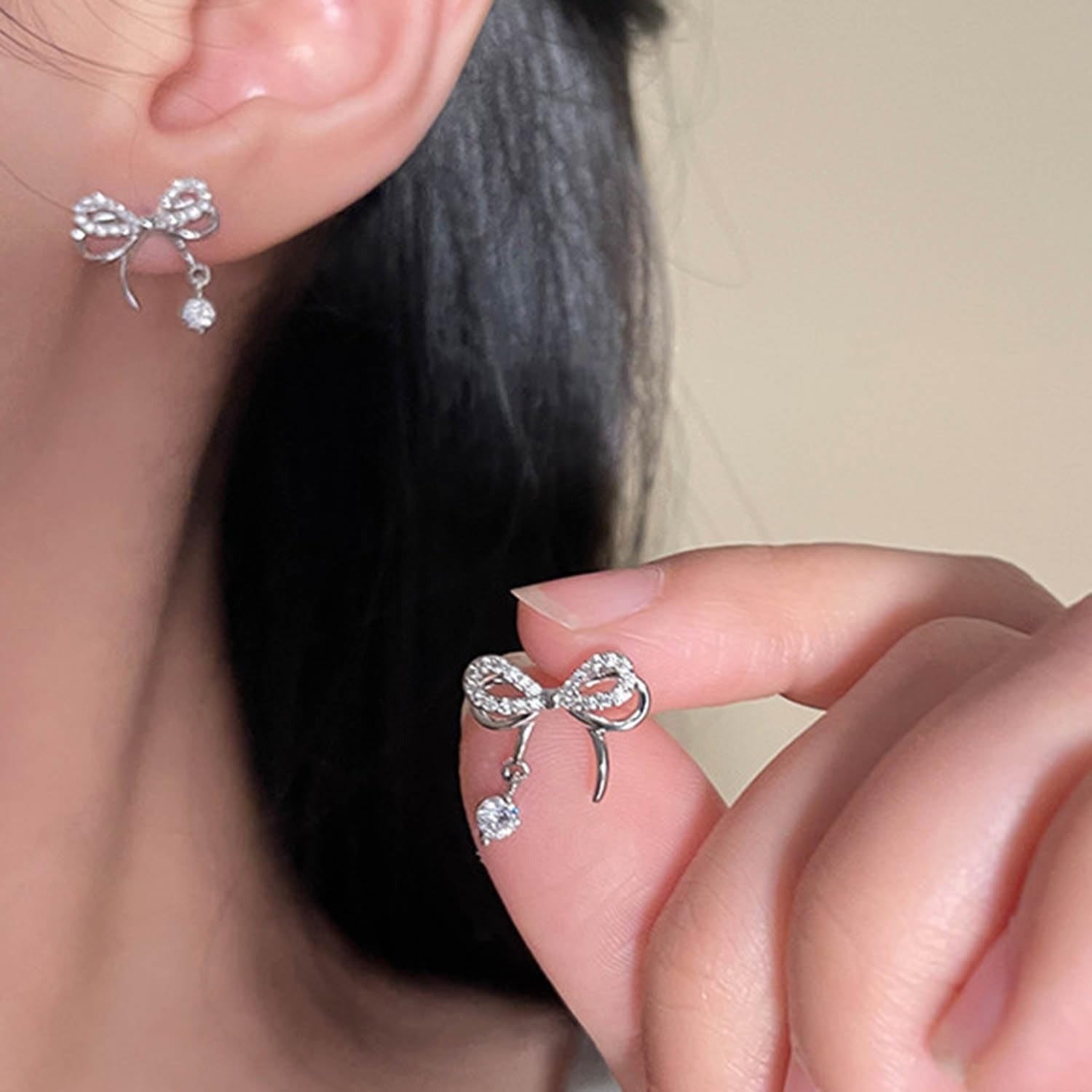 Silver Bow Earrings being worn and held up to the ear.