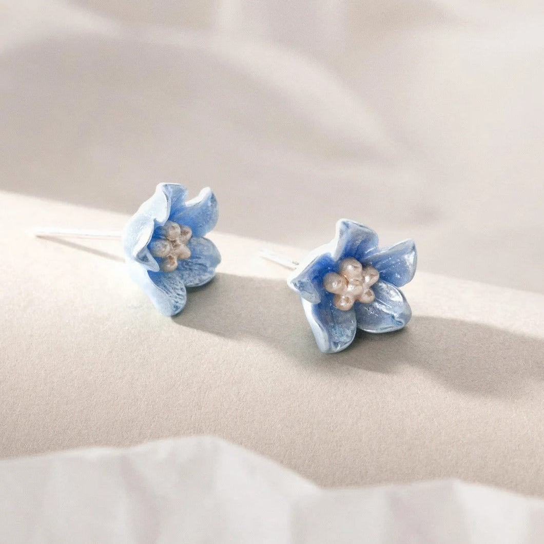 Pair of Blue Petal Blossom Earrings with pearl centers on a beige fabric background