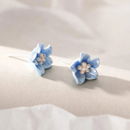 Pair of Blue Petal Blossom Earrings with pearl centers on a beige fabric background