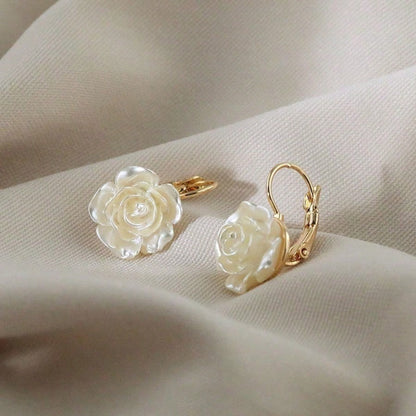 Pair of White Rose Earrings with white floral designs on a beige fabric background