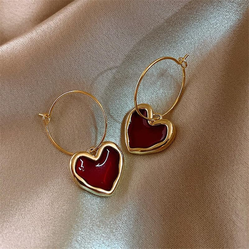 Ruby Heart Hoop Earrings with red heart charms on a beige fabric background