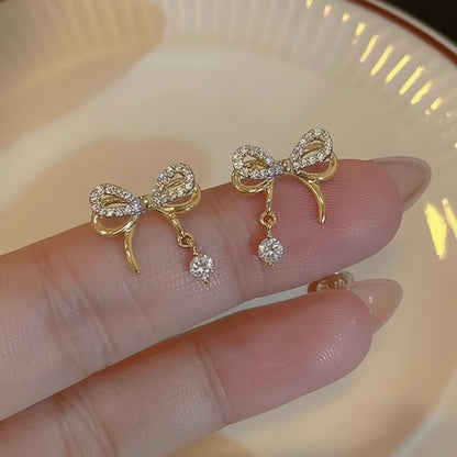 Sparkling Gold Crystal Bow Earrings on a finger against a neutral background