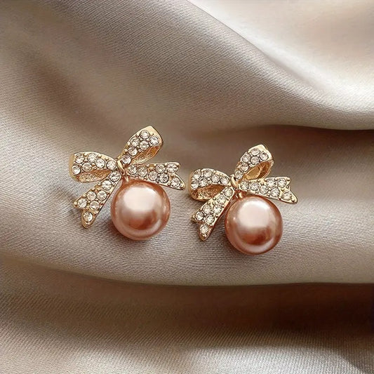 Pair of Peach Ornament Bow Earrings with pink pearls and gold bows on a soft fabric background