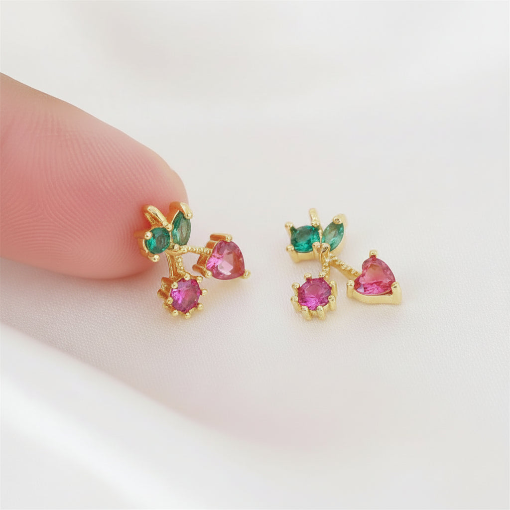Gold earrings with pink and green gemstones held between fingers on a light background