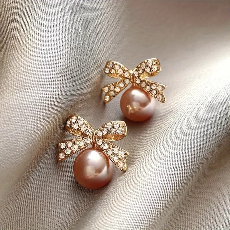 Peach Ornament Bow Earrings with gold bows on a light fabric background