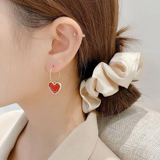 Close-up of a person wearing a Ruby Heart Hoop Earring and a beige scrunchie in their hair.