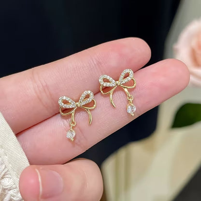 Sparkling Gold Crystal Bow Earrings held between fingers against a blurred background