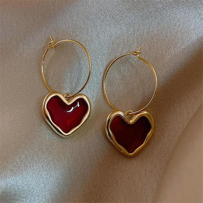 Ruby Heart Hoop Earrings with red heart charms on a beige fabric background