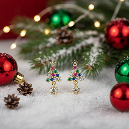 Twinkling Christmas Tree Earrings with gemstones on a snowy background with ornaments and lights.