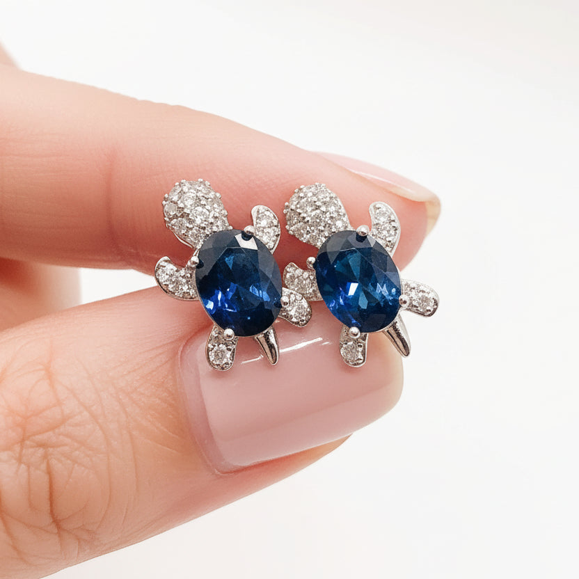 Blue Crystal Turtle Earrings with blue gemstones held between fingers on a white background