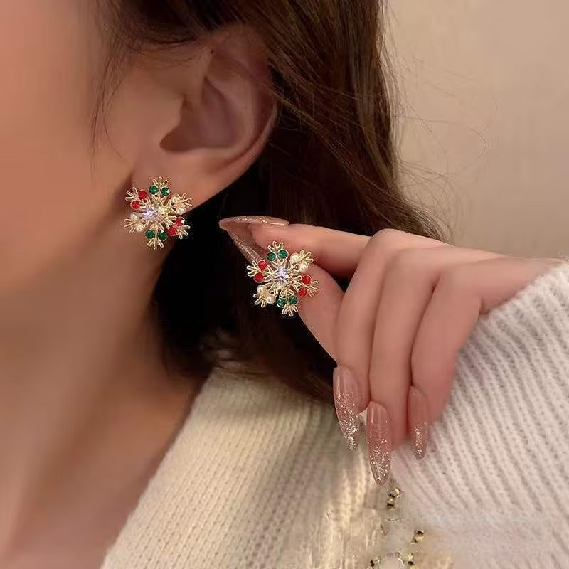 Close-up of a person wearing snowflake-shaped earrings with red and green accents.