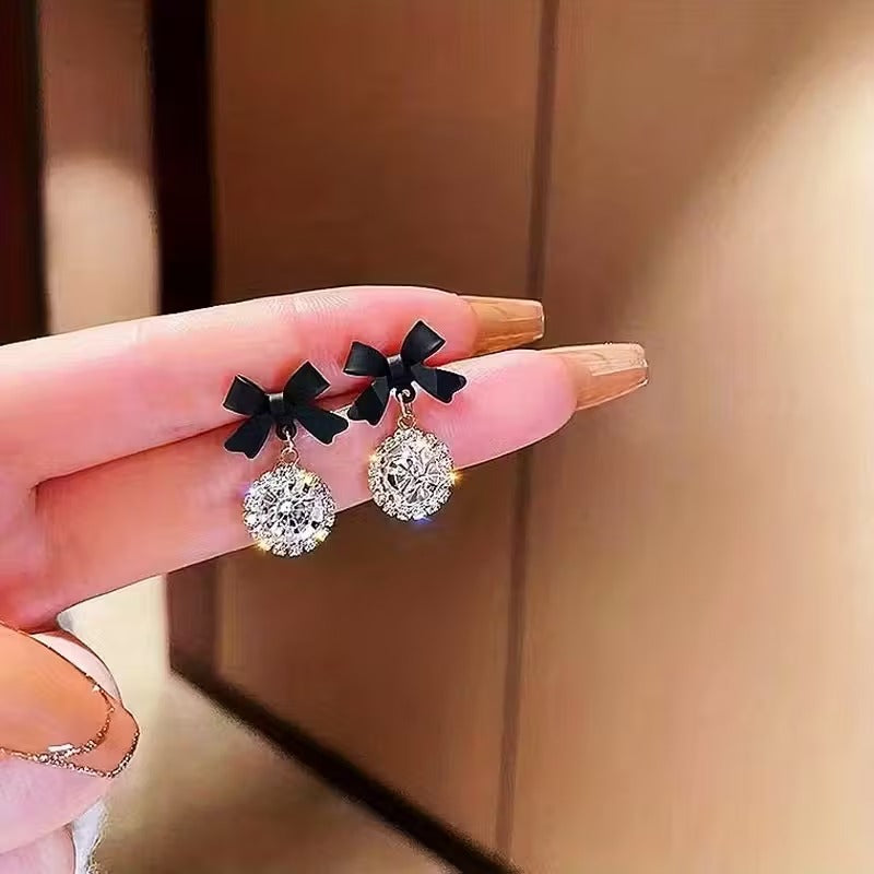 Woman holding Black Bow Crystal Drop Earrings between fingers against a neutral background