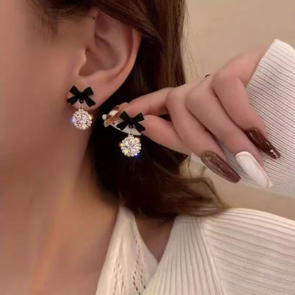 Close-up of a woman wearing and holding up a pair of the Black Bow Crystal Drop Earrings.