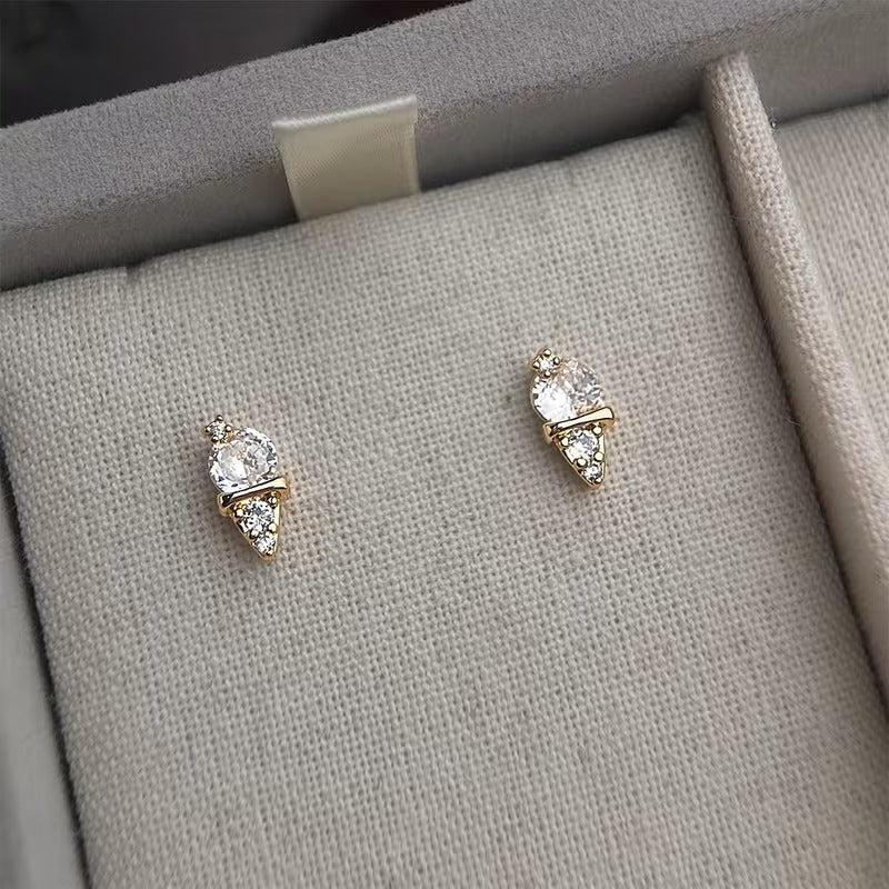 Pair of gold earrings with clear stones on a gray fabric surface