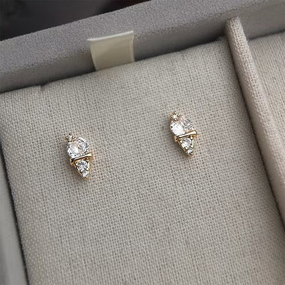 Pair of gold earrings with clear stones on a gray fabric surface