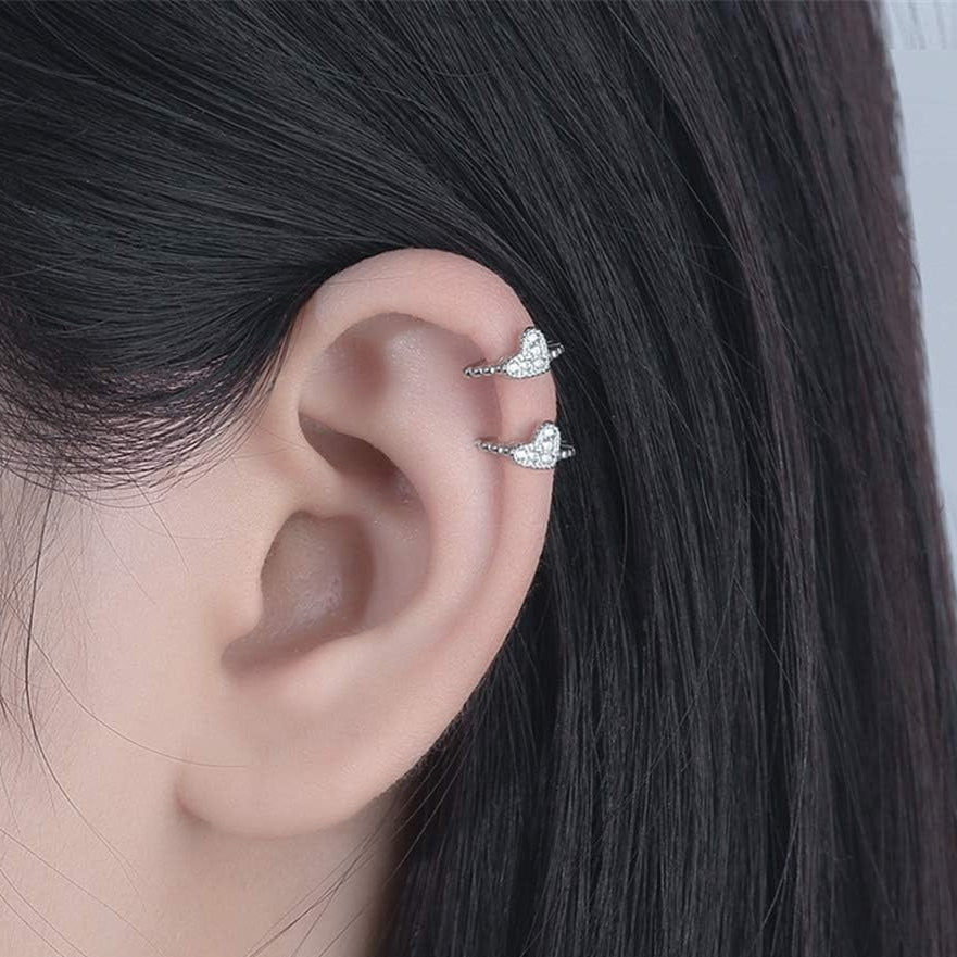 Close-up of an ear wearing two Silver Tiny Crystal Heart Earrings with a plain background