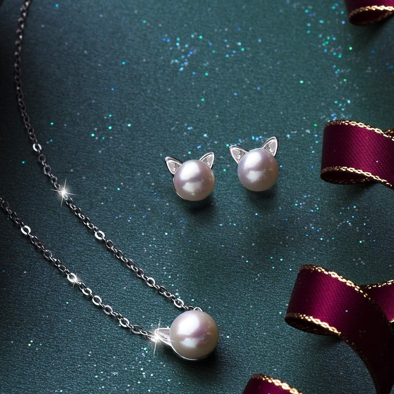 Pearl Cat Earrings with Pearl Cat Necklace on a dark green surface with ribbons.