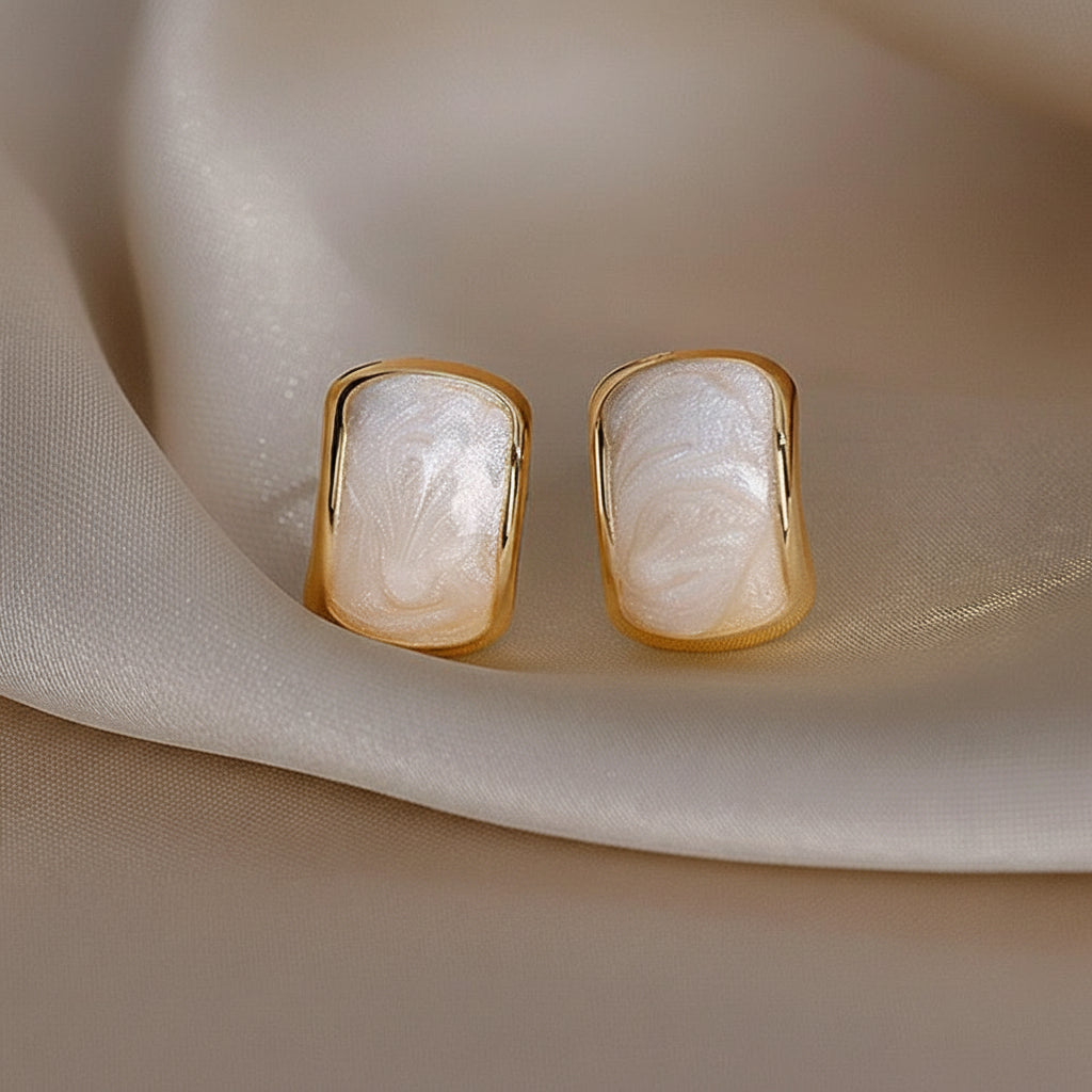 Gold-Trim Mother-of-Pearl Earrings with a textured white stone on a beige fabric background