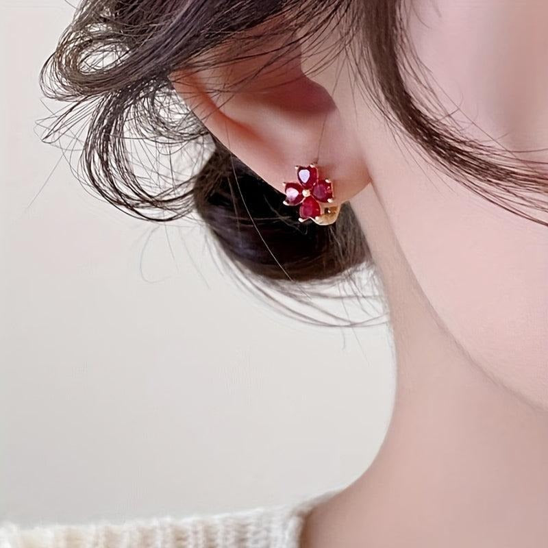 Close-up of an ear wearing a Ruby Red Flower Petal Hoop Earring with a red gemstone on a neutral background