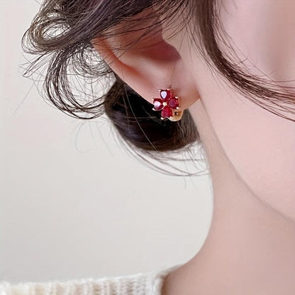 Close-up of an ear wearing a Ruby Red Flower Petal Hoop Earring with a red gemstone on a neutral background
