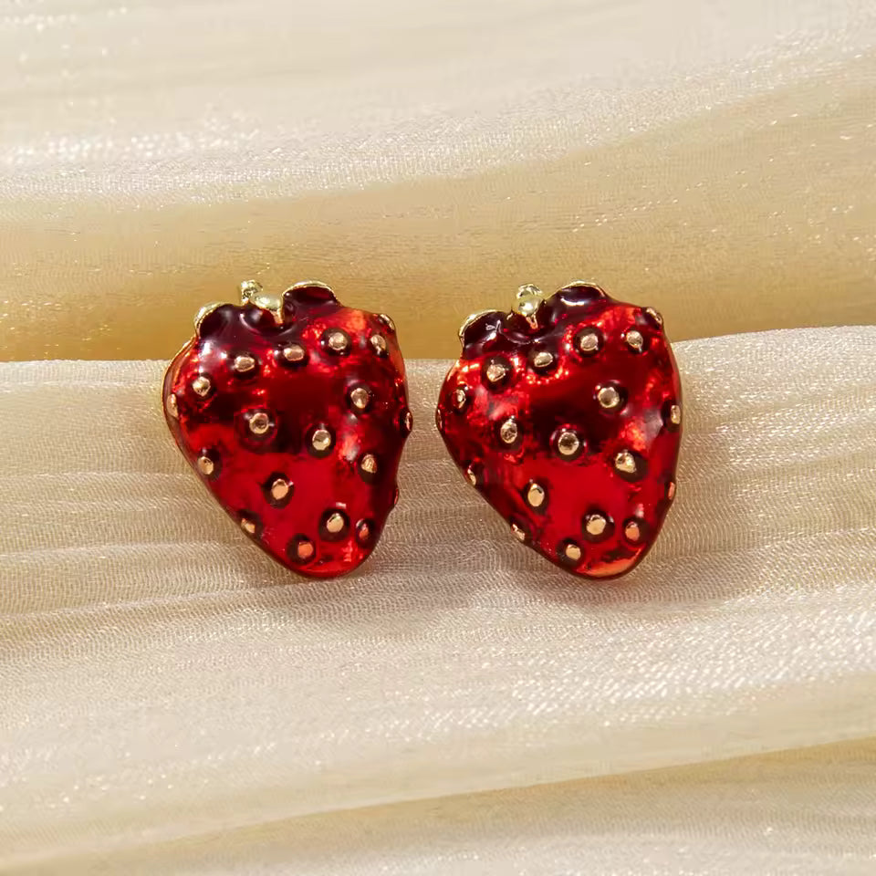 Ruby Red Strawberry Earrings with gold accents on a beige fabric background