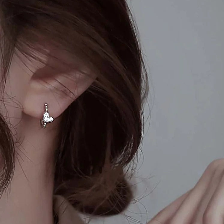 Close-up of an ear with a Silver Tiny Crystal Heart Earrings against a neutral background