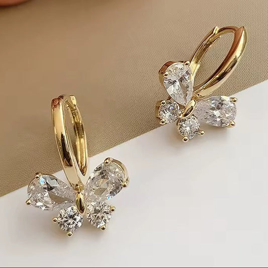 Gold butterfly-shaped earrings with clear gemstones on a beige and white background