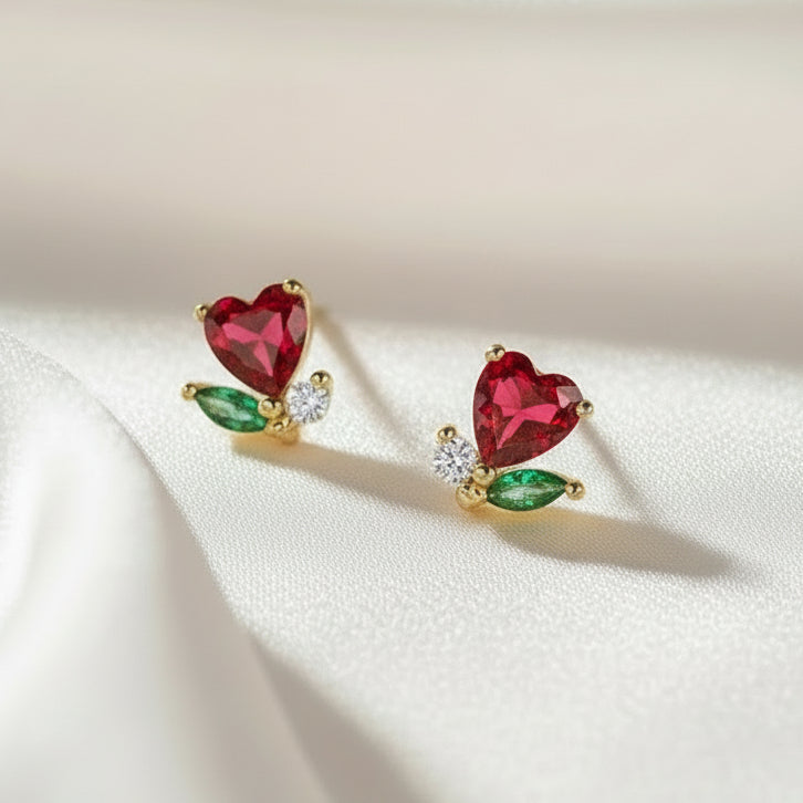 Pair of gold Mini Ruby Heart Blossom Earrings with red heart-shaped gemstones on a beige background