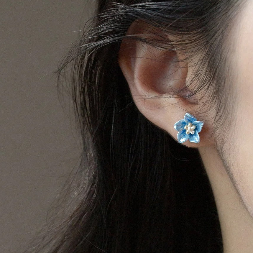 Close-up of a person wearing a blue floral earring against a neutral background