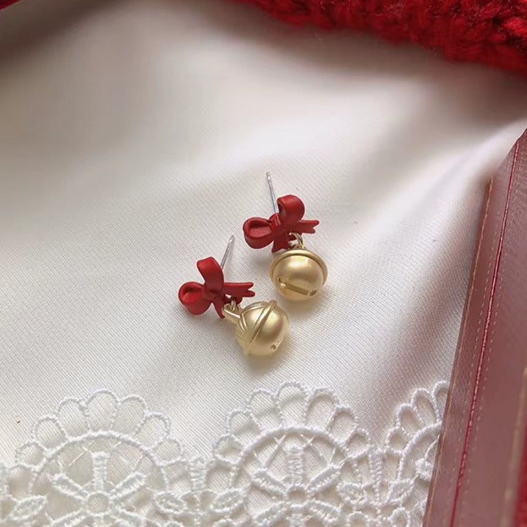 Jingle Bell Bow Earrings on a white fabric background with red ribbons.