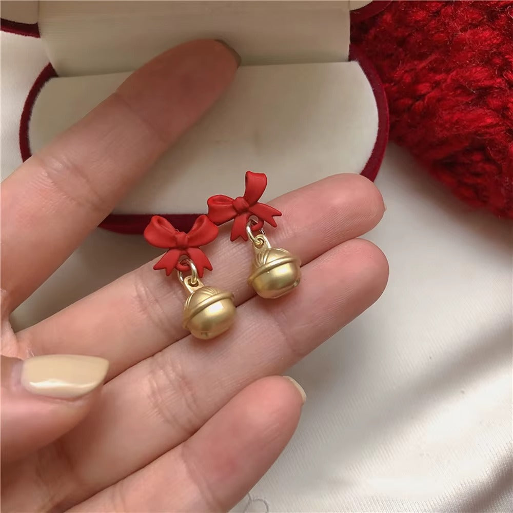 Jingle Bell Bow Earrings held between fingers on a white background