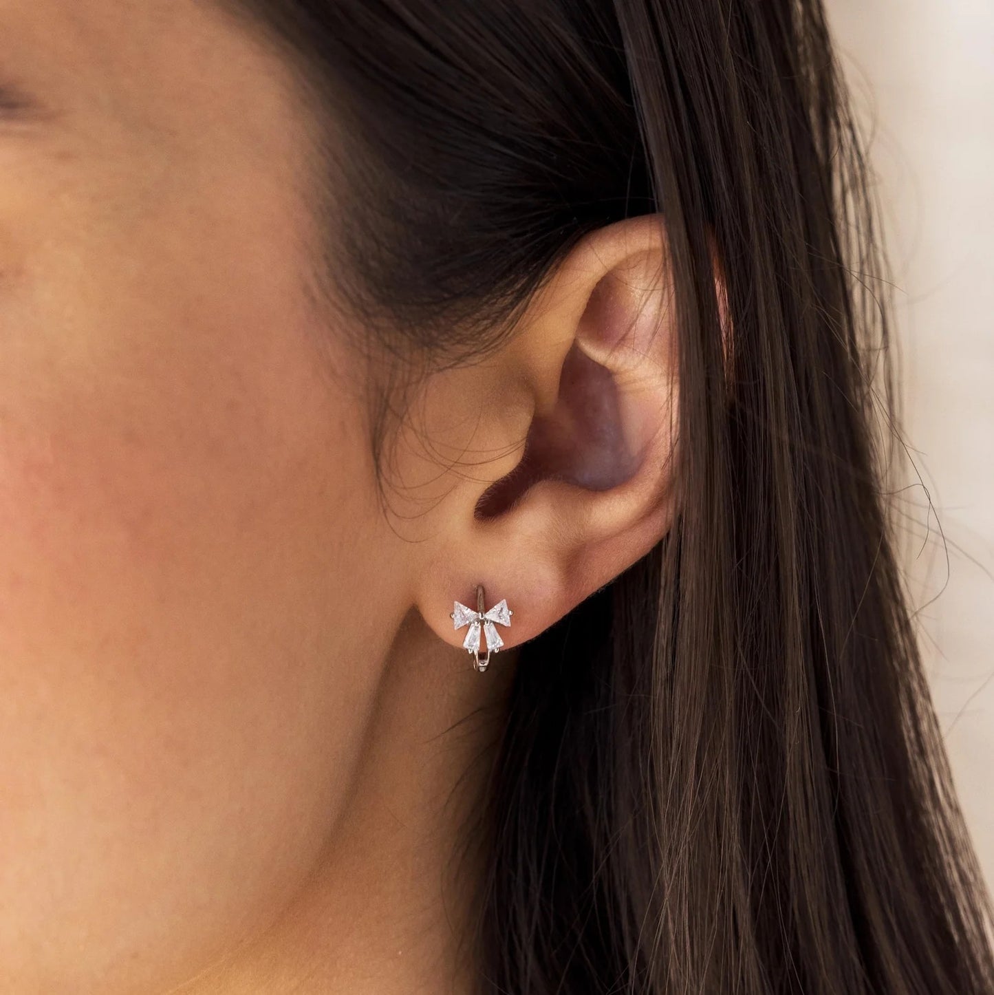 Close-up of an ear wearing Tiny Crystal Ribbon Earrings with a neutral background